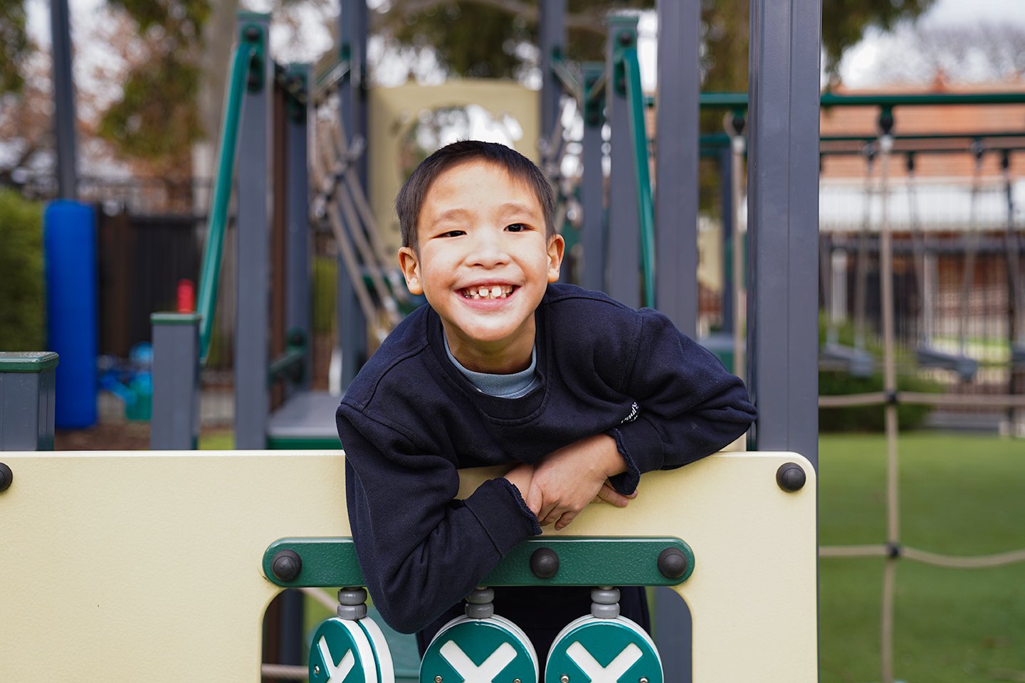 Boy smiling at the camera whilst on playground equipment wearing a navy school uniform