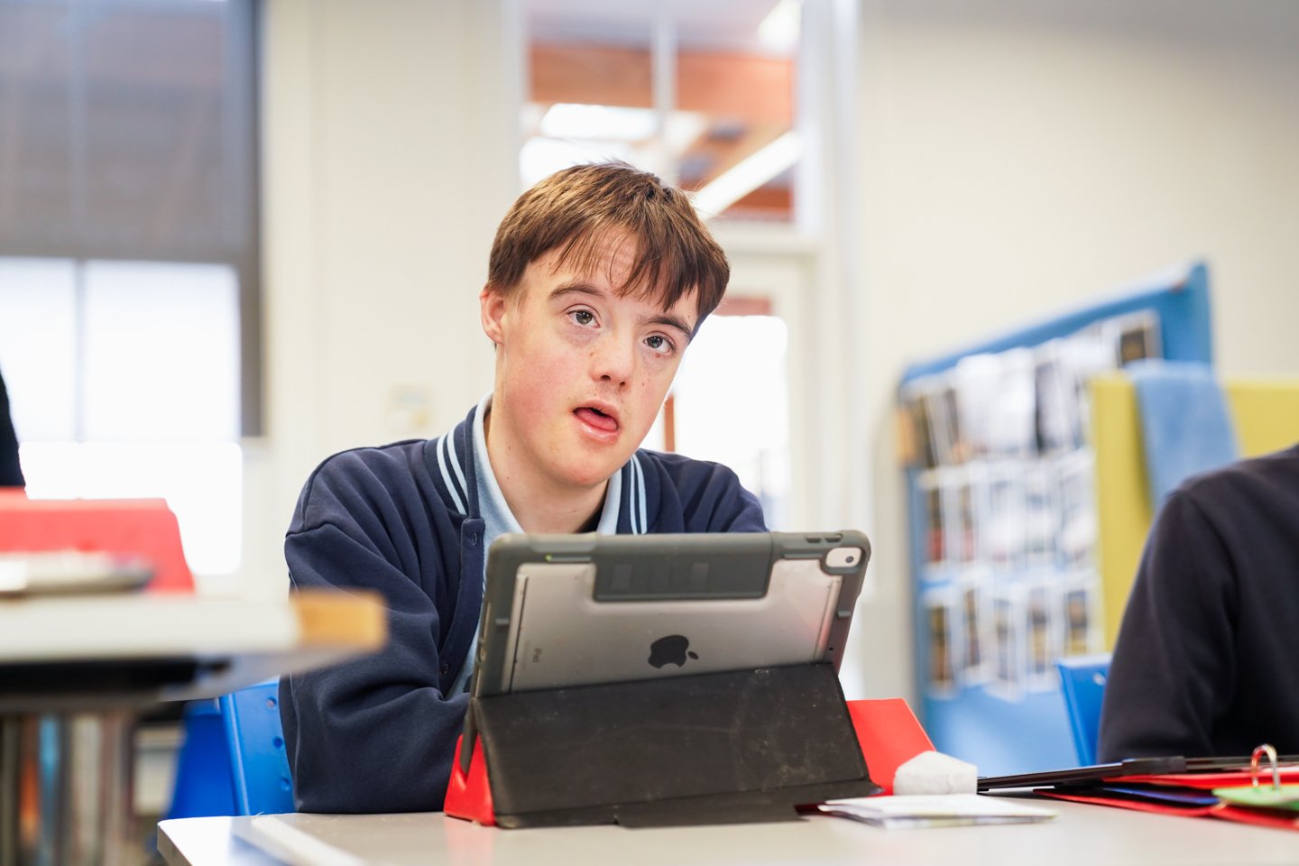 A male student wearing a navy school uniform with an iPad in front of him.