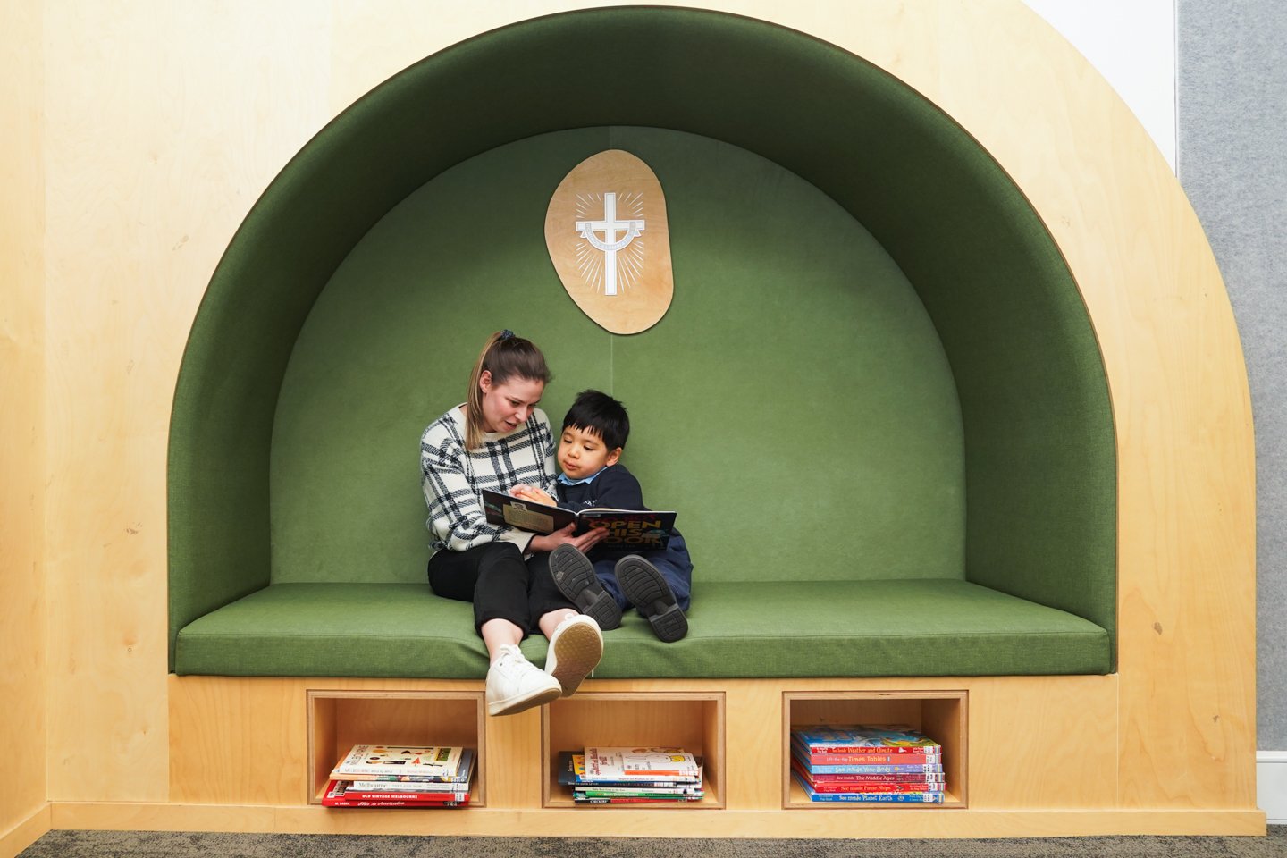 Female reading a book to a small male child in a green reading nook with the cross symbol above them